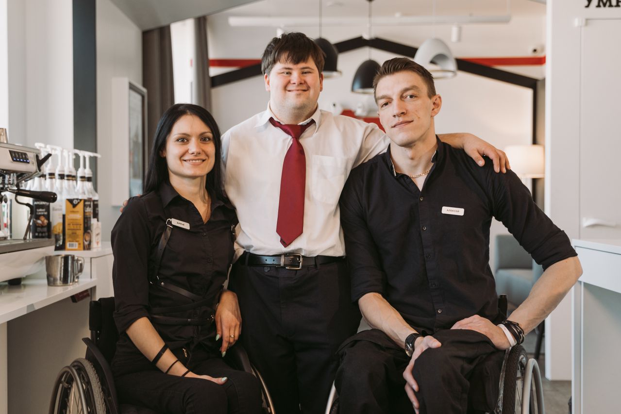 Three adults together in a café, including two people using wheelchairs.